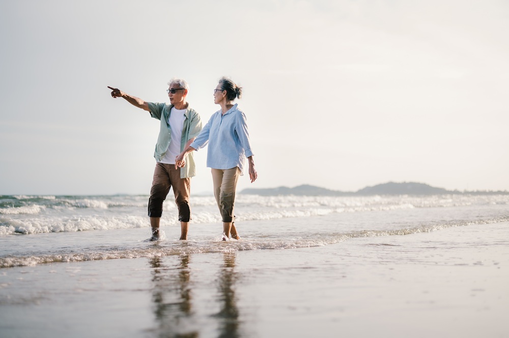 Elderly Asian couple walking on the beach at sunset